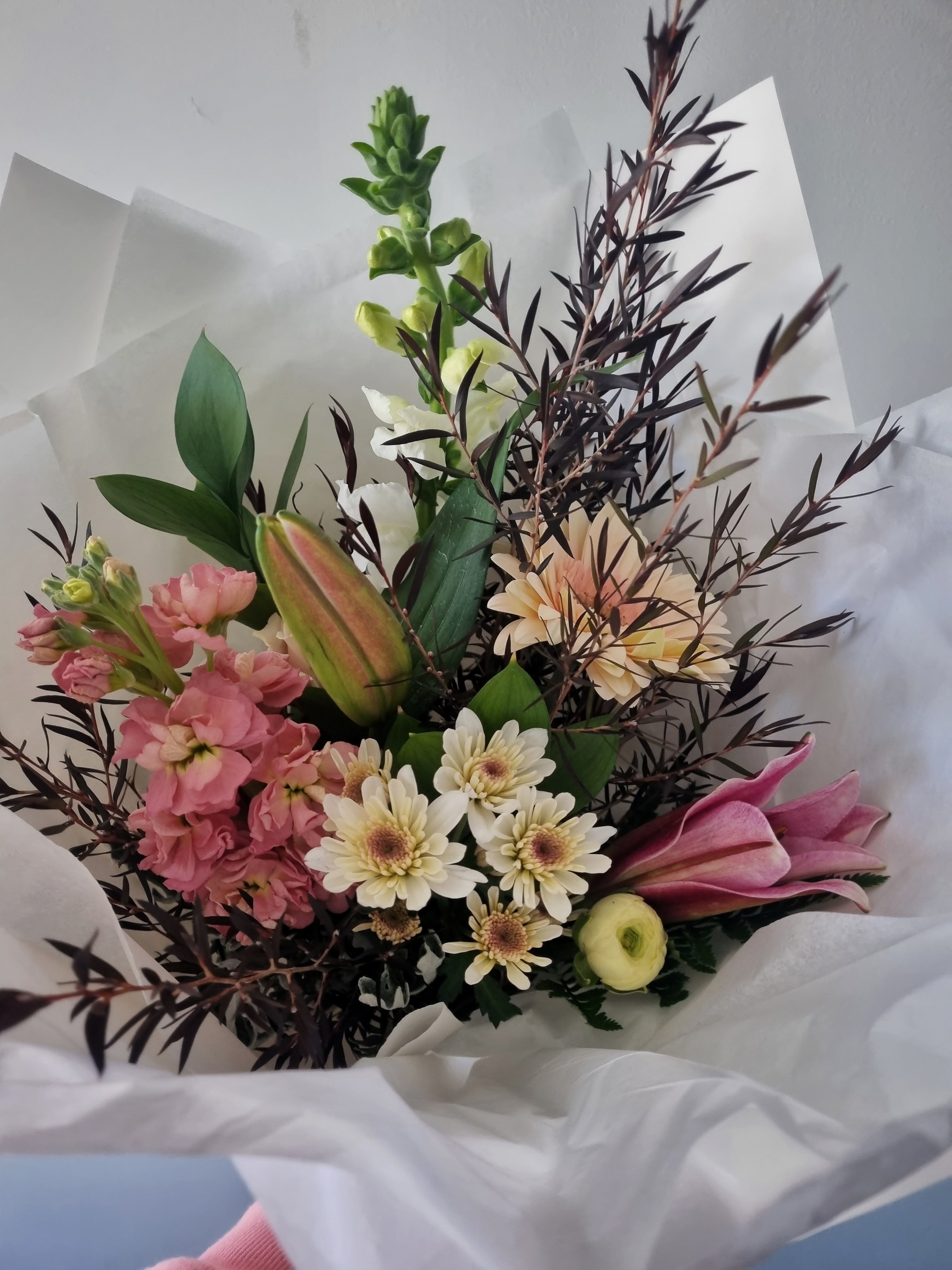 Vintage Bouquet with soft pink and yellow flowers and dark foliage, wrapped in white tissue paper.