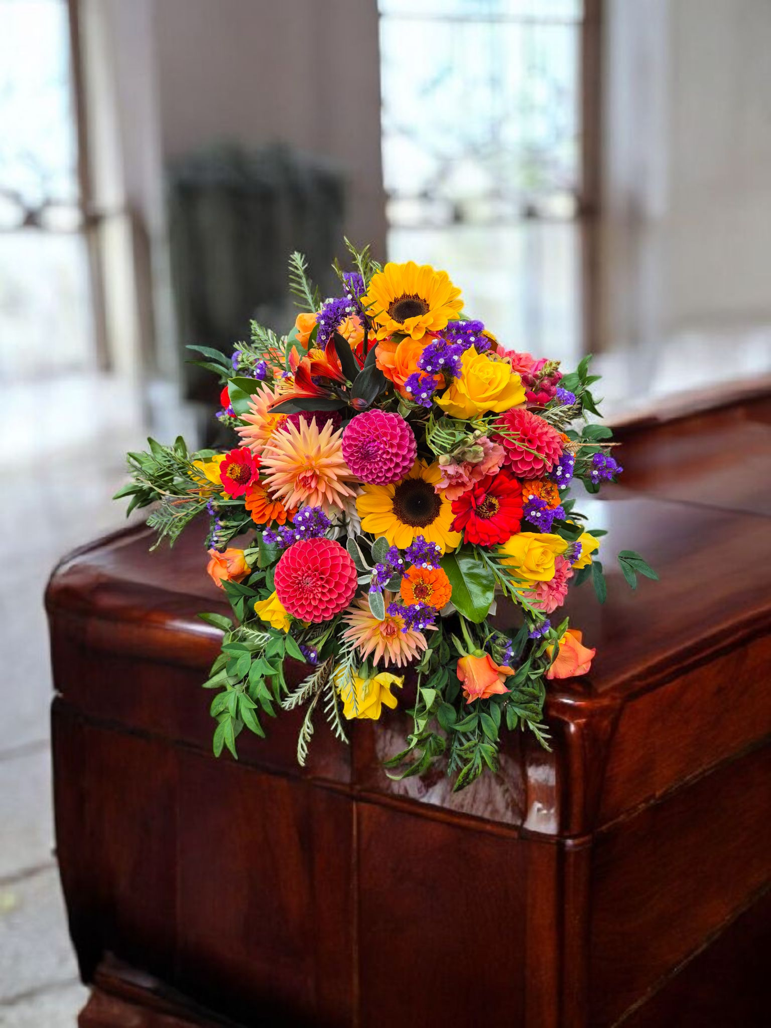 Casket Sheaf floral arrangement for funerals and memorials, lovingly made with vibrant orange, pink and yellow flowers and foliage.