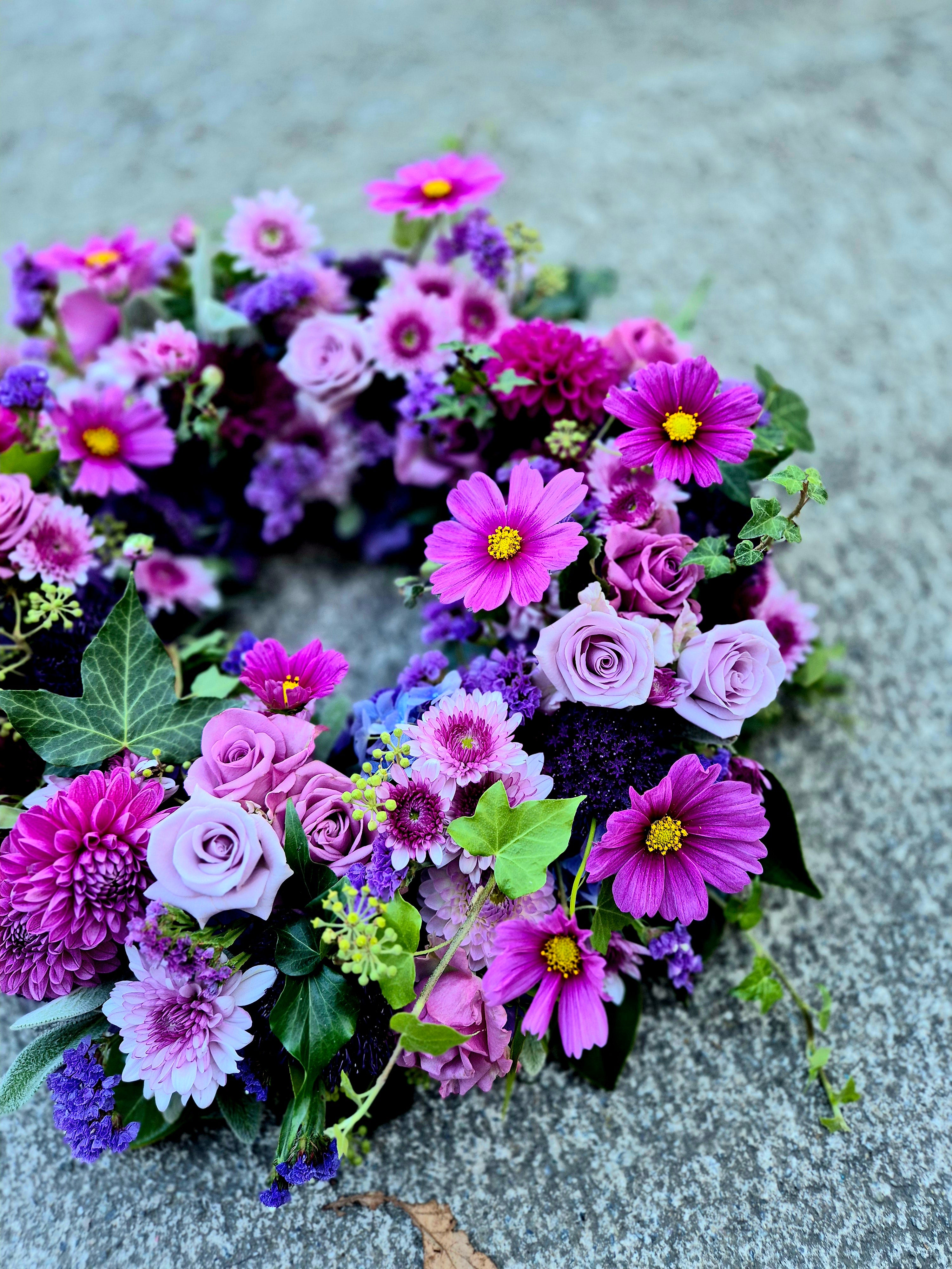 Wreath of Remembrance for funerals and memorials made with vibrant purple and pink flowers and lush foliage.