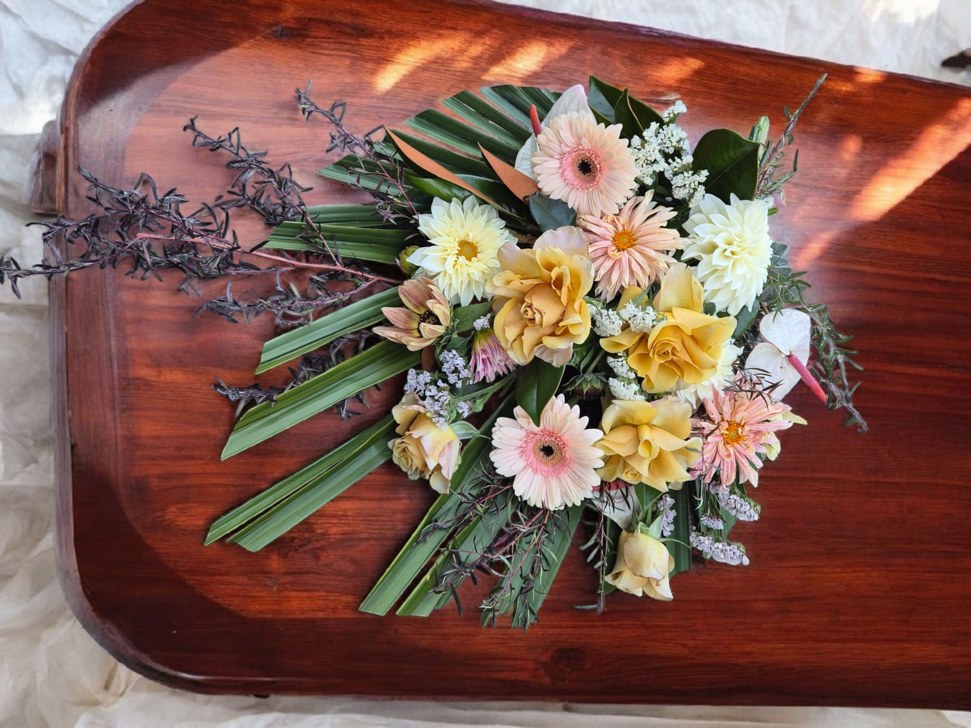 Casket Sheaf floral arrangement for funerals and memorials, lovingly made with soft yellow, pink and cream flowers and foliage.
