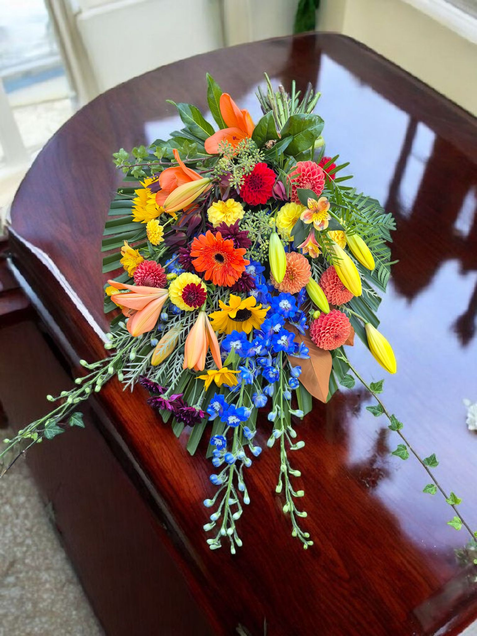 Casket Sheaf floral arrangement for funerals and memorials, lovingly made with vibrant orange, purple and yellow flowers and foliage.