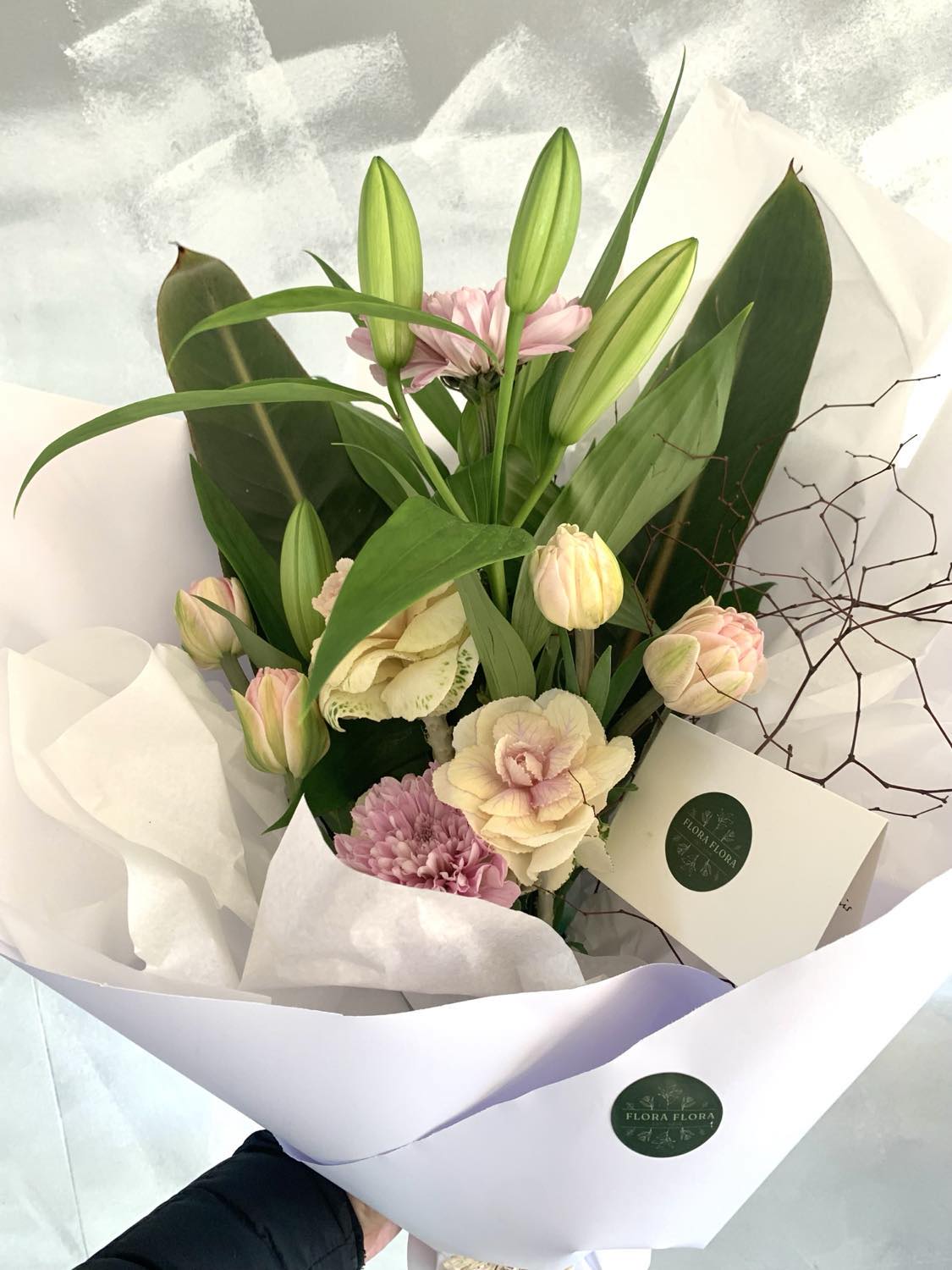 Sympathy Bouquet with white and pastel flowers wrapped with foliage in white paper.