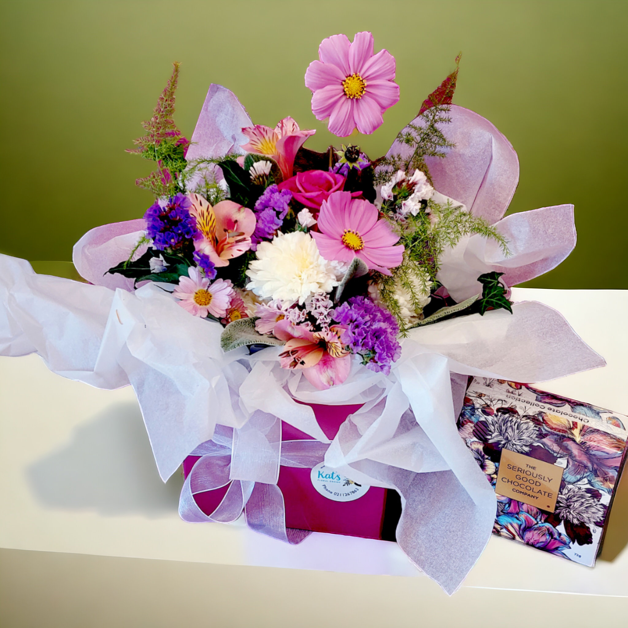 Posy of vibrant pink, purple and white flowers, arranged in a pink box with ribbon and tissue paper.