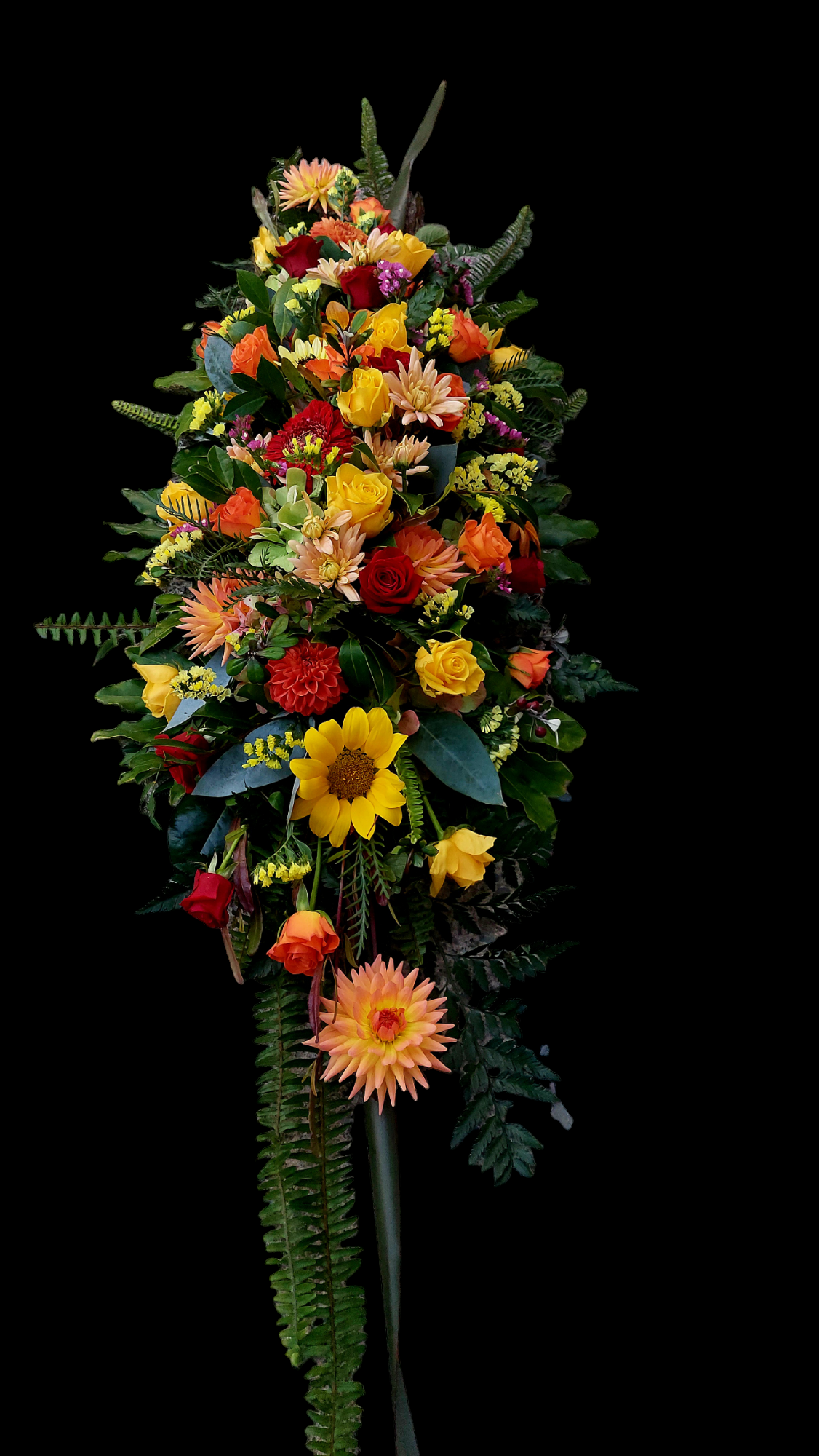 Bright Casket Spray for funerals and memorials made with an assortment of brightly coloured warm-toned flowers and foliage.
