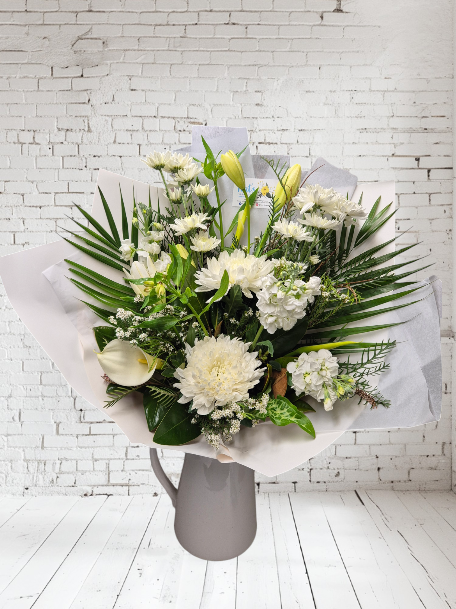 Ivory Whites floral bouquet made with a variety of white and cream flowers and green foliage, wrapped in matching tissue paper.