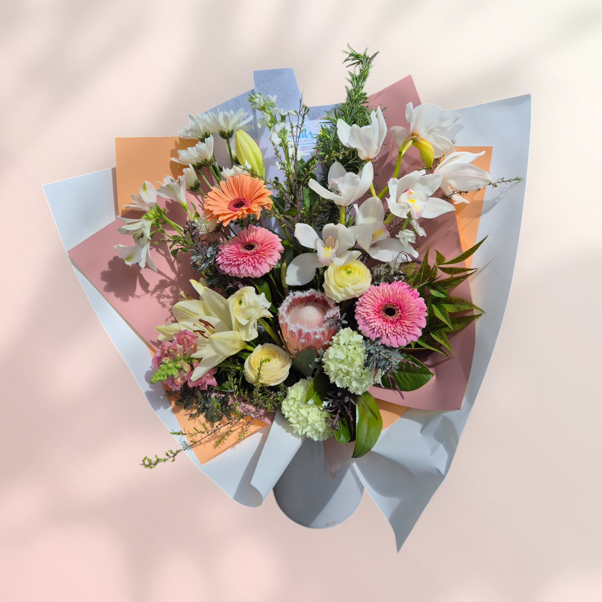 Pastel-Licious floral bouquet made with pink, peach and white flowers, wrapped in matching tissue paper.