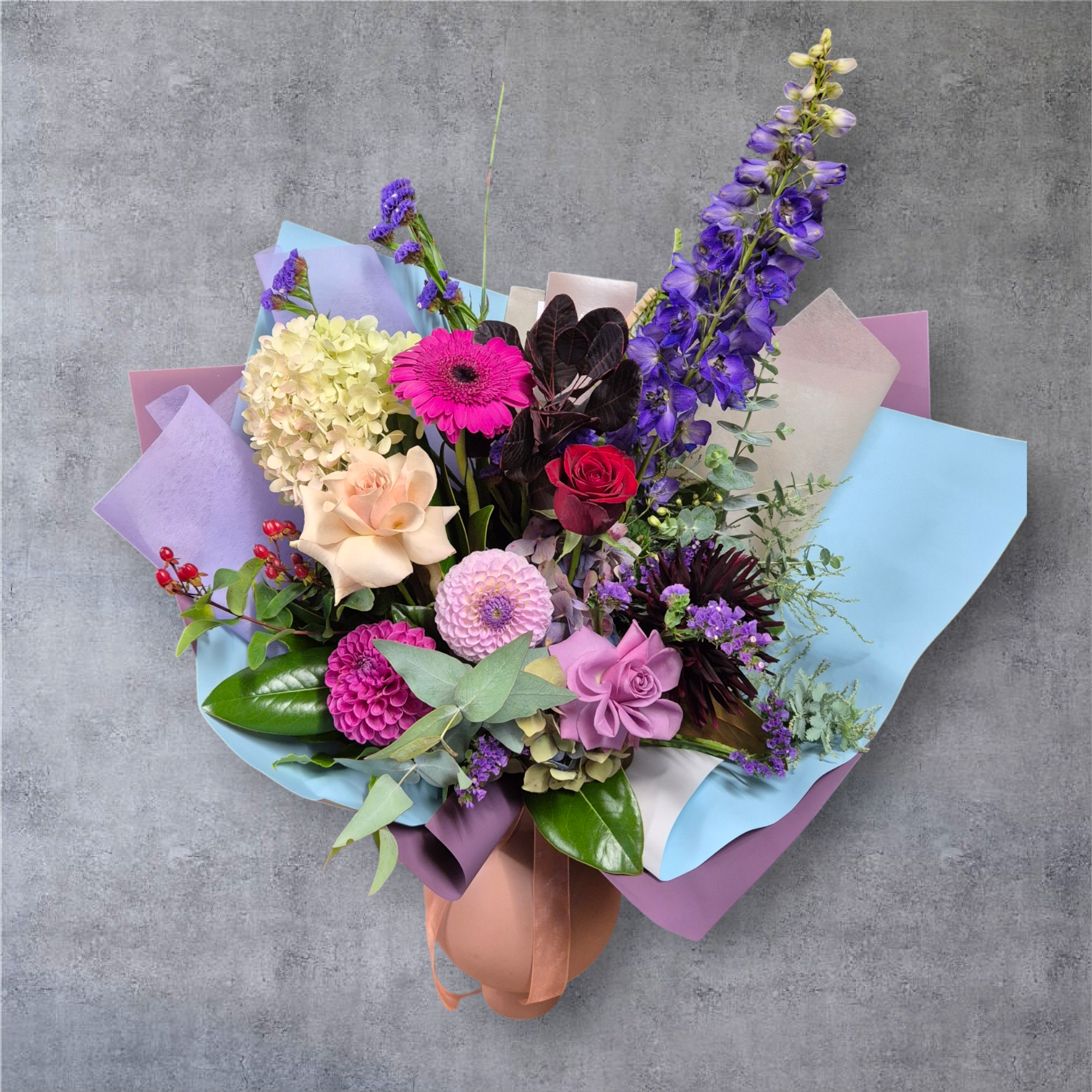 Seasonal Large Bouquet - Florist Choice with purple and pink flowers wrapped in purple and white tissue paper.