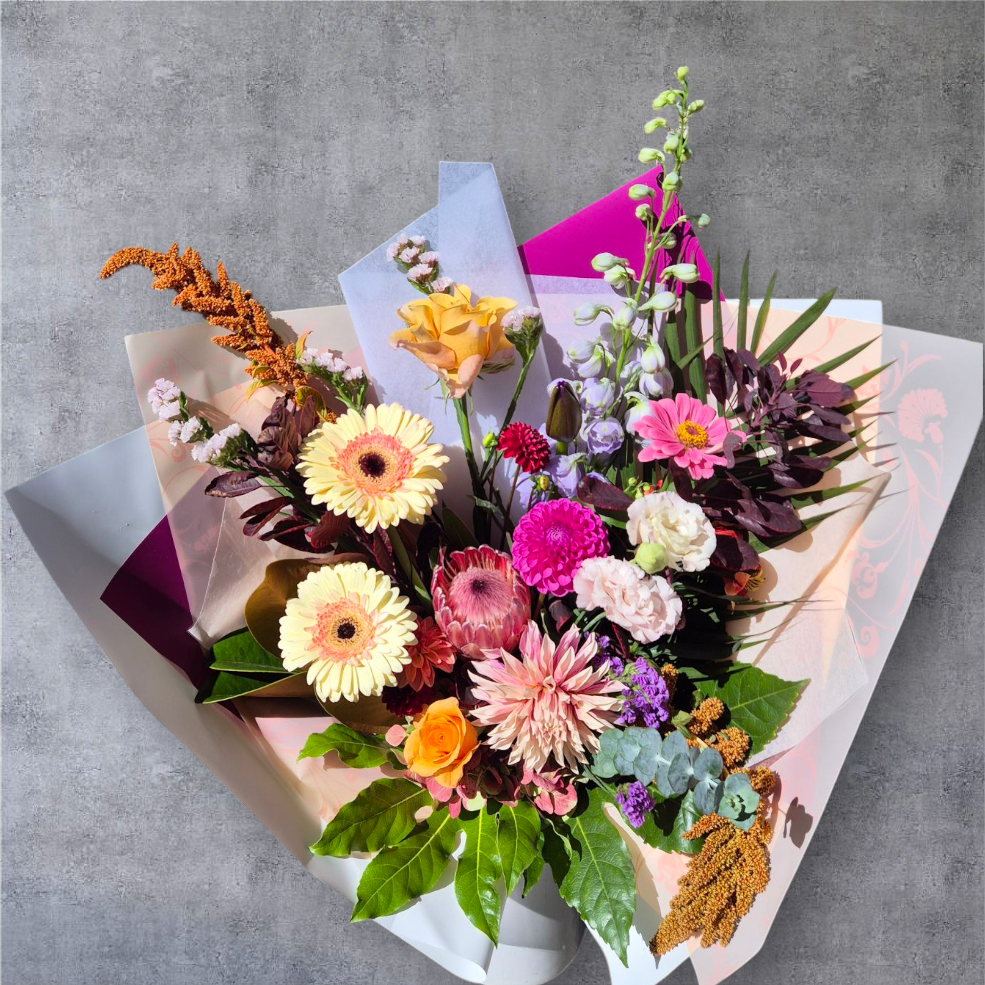 Seasonal Large Bouquet - Florist Choice with pink, purple and yellow flowers wrapped in matching tissue paper.