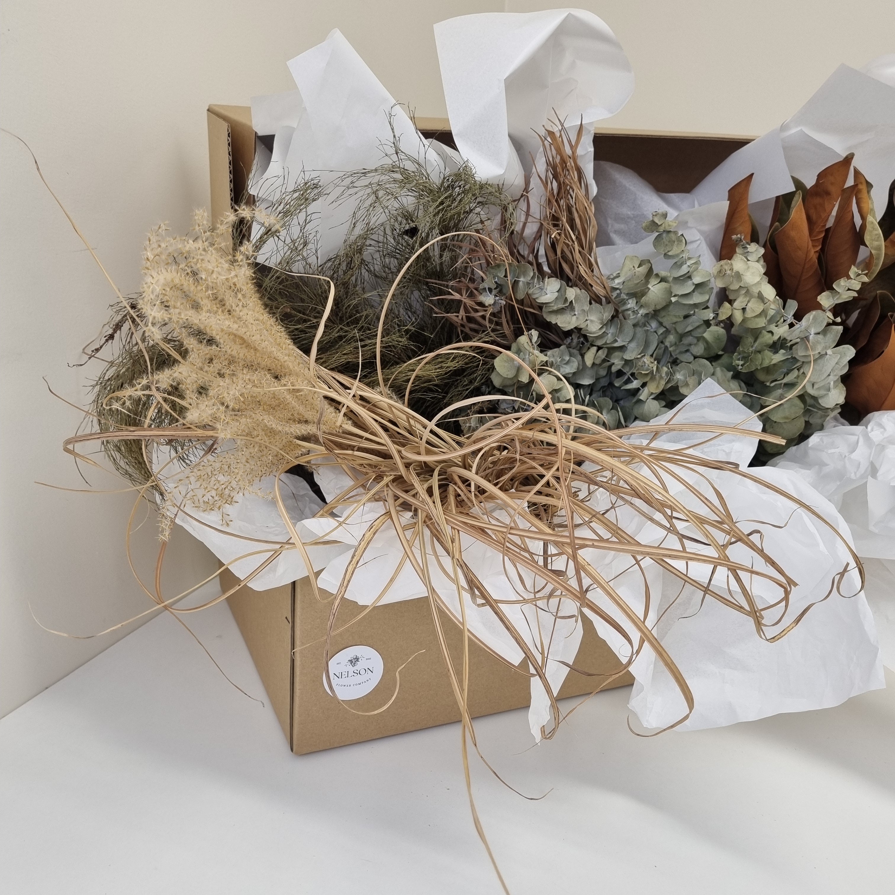 Dried Foliage Box filled with various preserved greenery, in a cardboard box with white tissue paper.