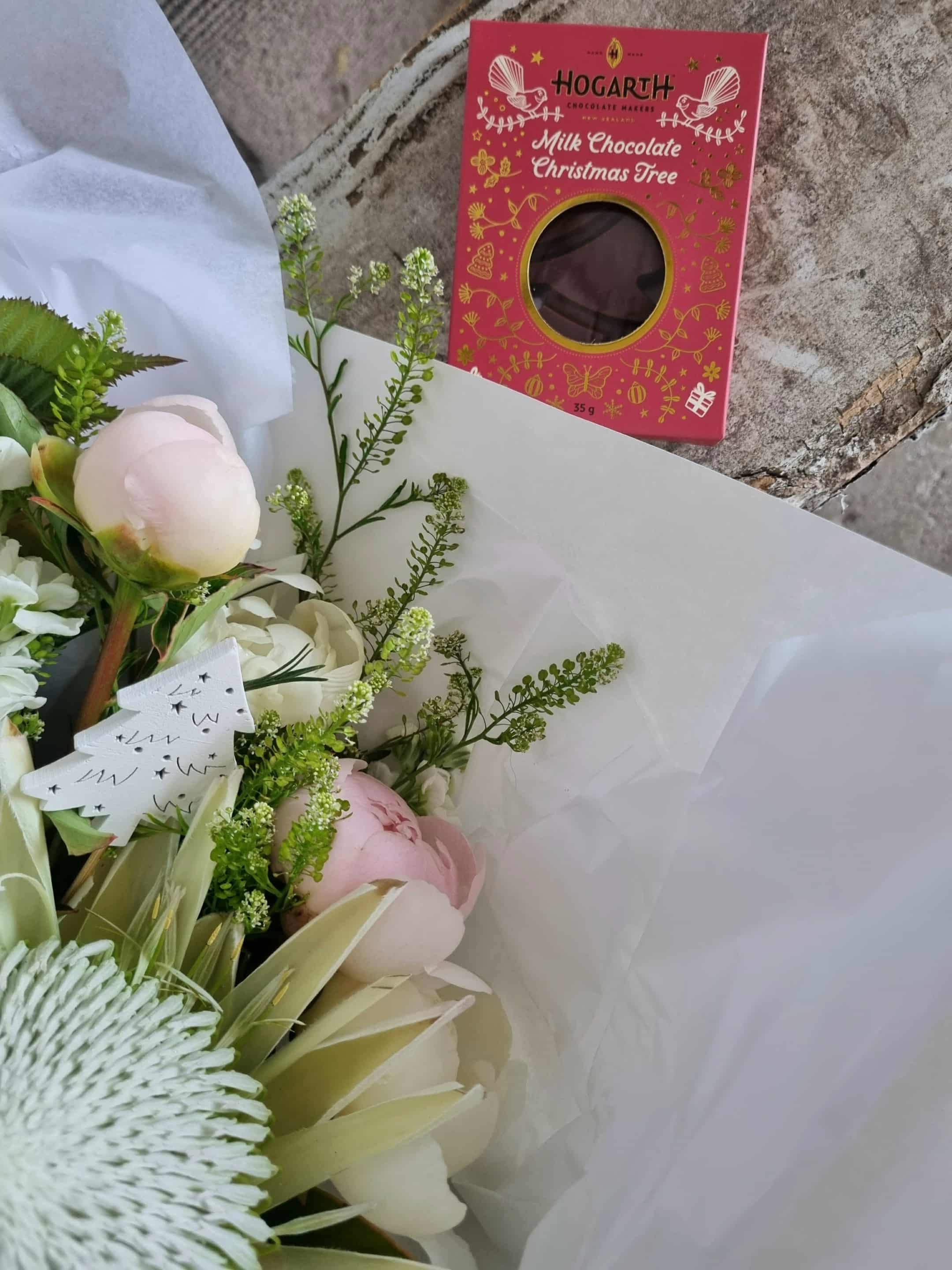 White Christmas bouquet made with white and rosy pink flowers and foliage, wrapped in matching paper. Complete with chocolate and Christmas ornament.