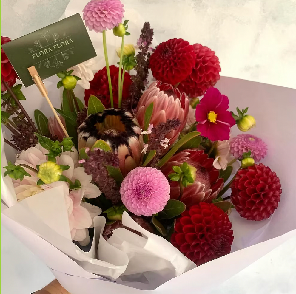 Protea Bouquet made with proteas and complimentary flowers in a variety of colours, wrapped in white paper.