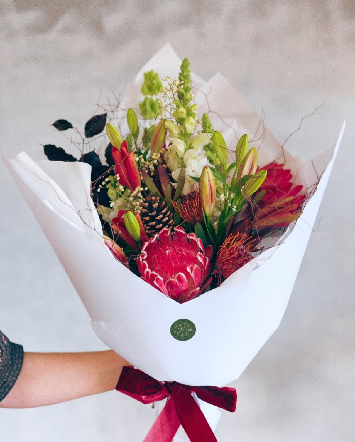 Flora Christmas bouquet made with red, orange and white flowers, wrapped in white paper and tied with a festive red ribbon.