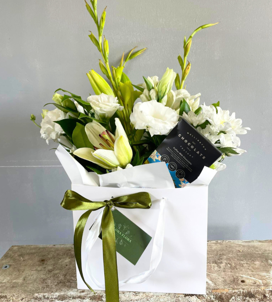 Bright White & Chocs gift basket with white flowers and Coffee Milk Chocolate from Wellington Chocolate Factory, presented in a white gift bag tied with green ribbon.