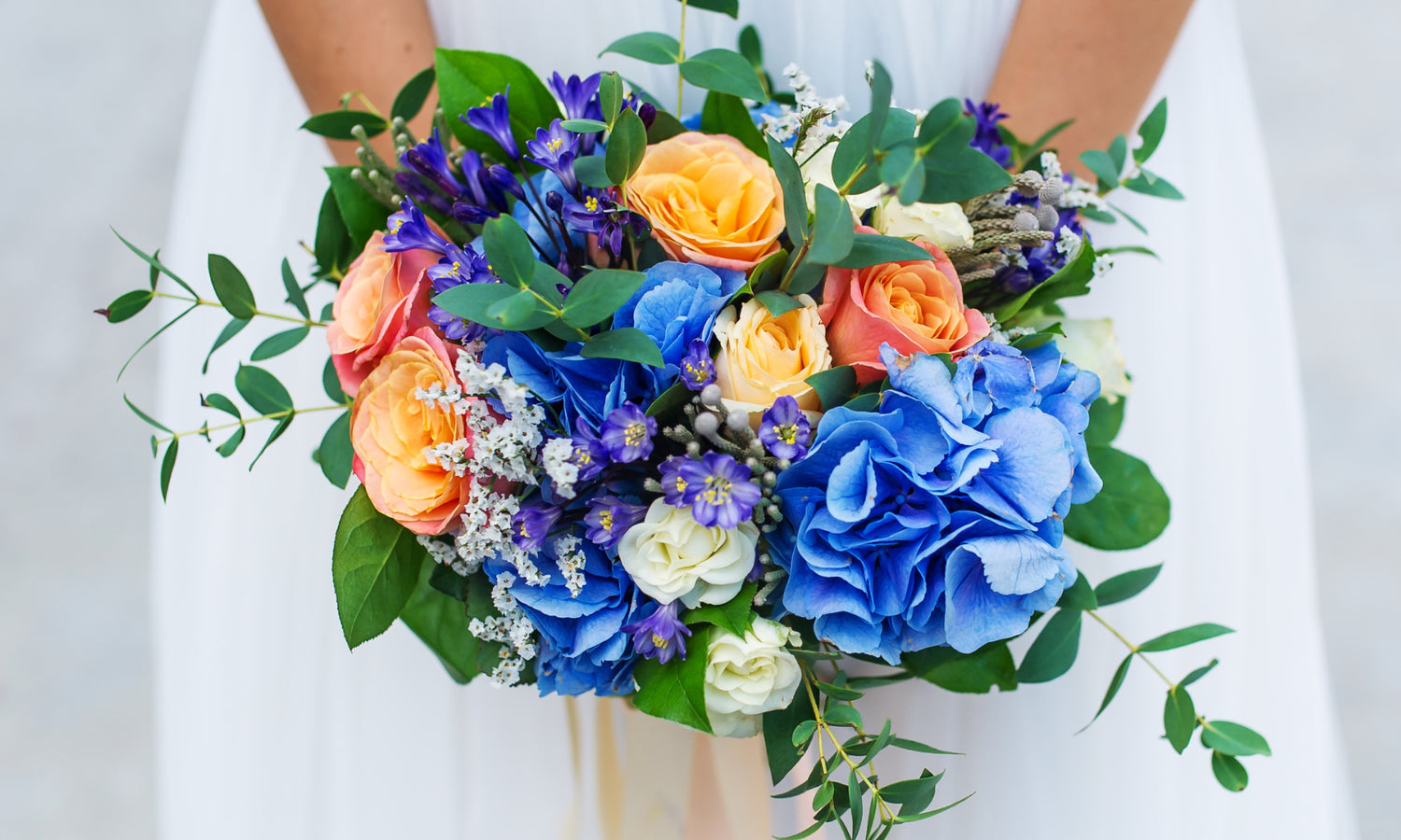 A bride in a white wedding dress holds her floral bouquet made with trendy vibrant coloured flowers in blue, purple and orange.