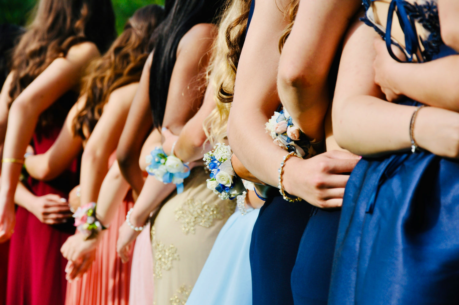 Teenage girls lined up with their arms around each other at prom, with flower corsages on their wrists.Photo by Todd Cravens on Unsplash.