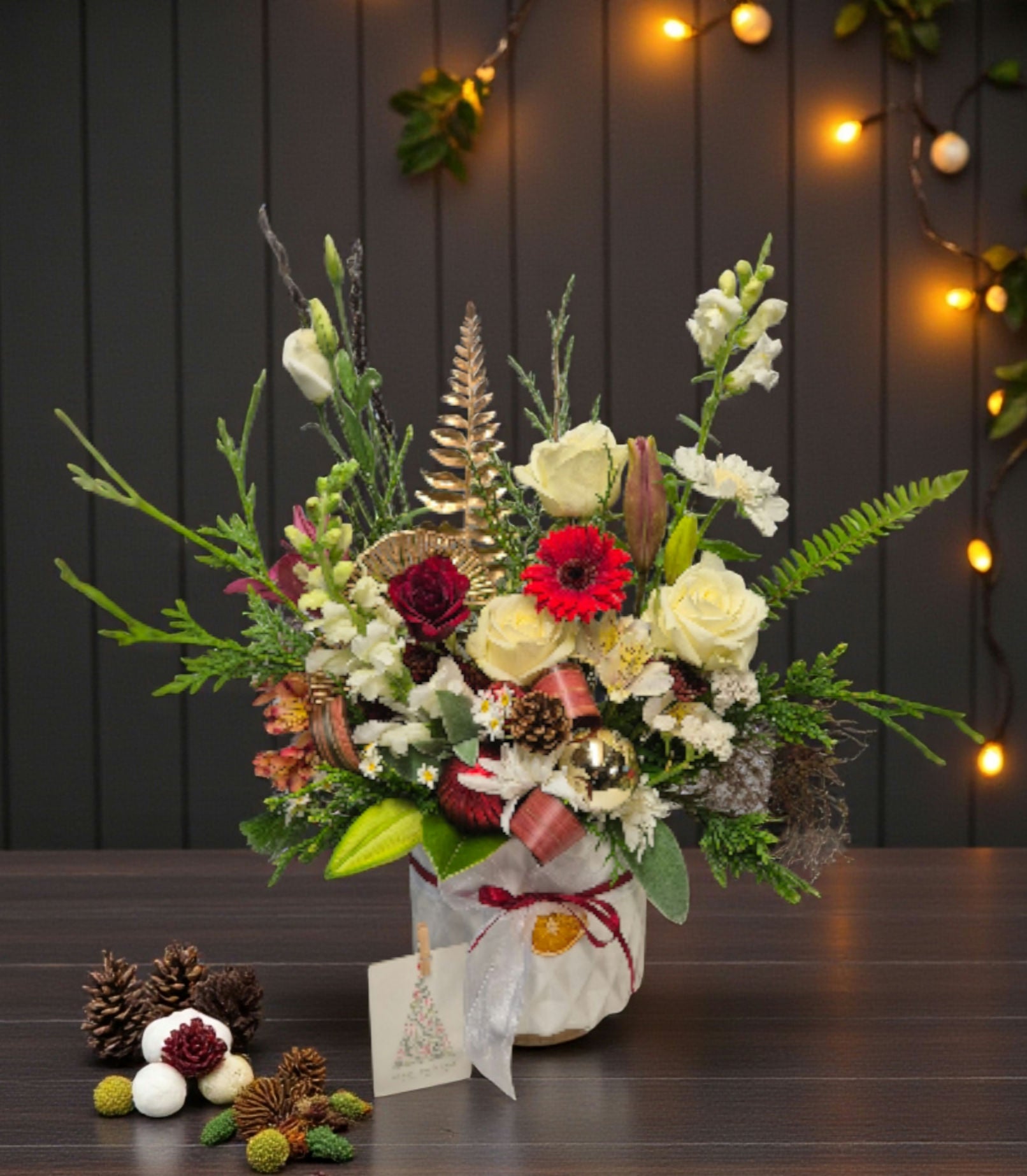 Deluxe Fresh Christmas Flower Arrangement made with festive red, white and green flowers and foliage, presented in a white ceramic vase and tied with a red ribbon.
