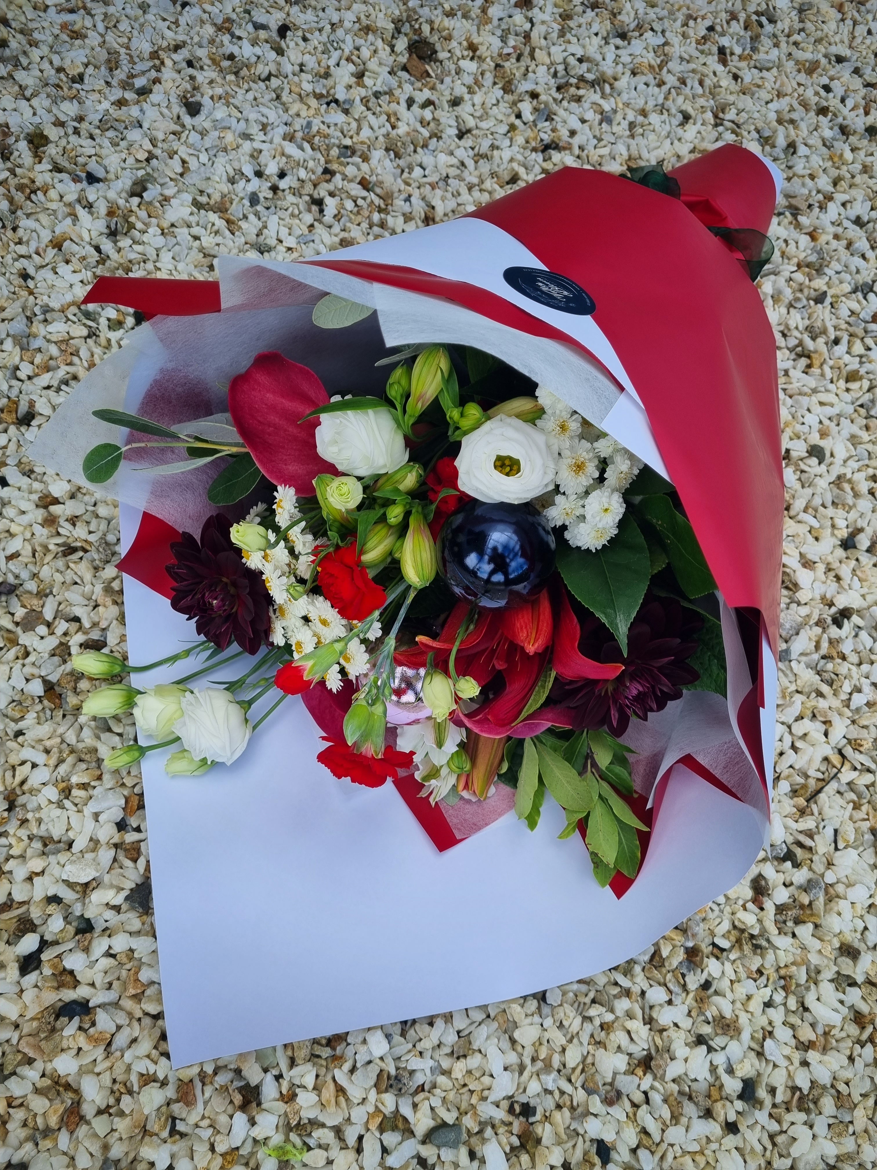 Xmas Bouquet made from a variety of white and red flowers and dark green foliage complete with Christmas baubles, wrapped in matching festive paper and tied with ribbons.