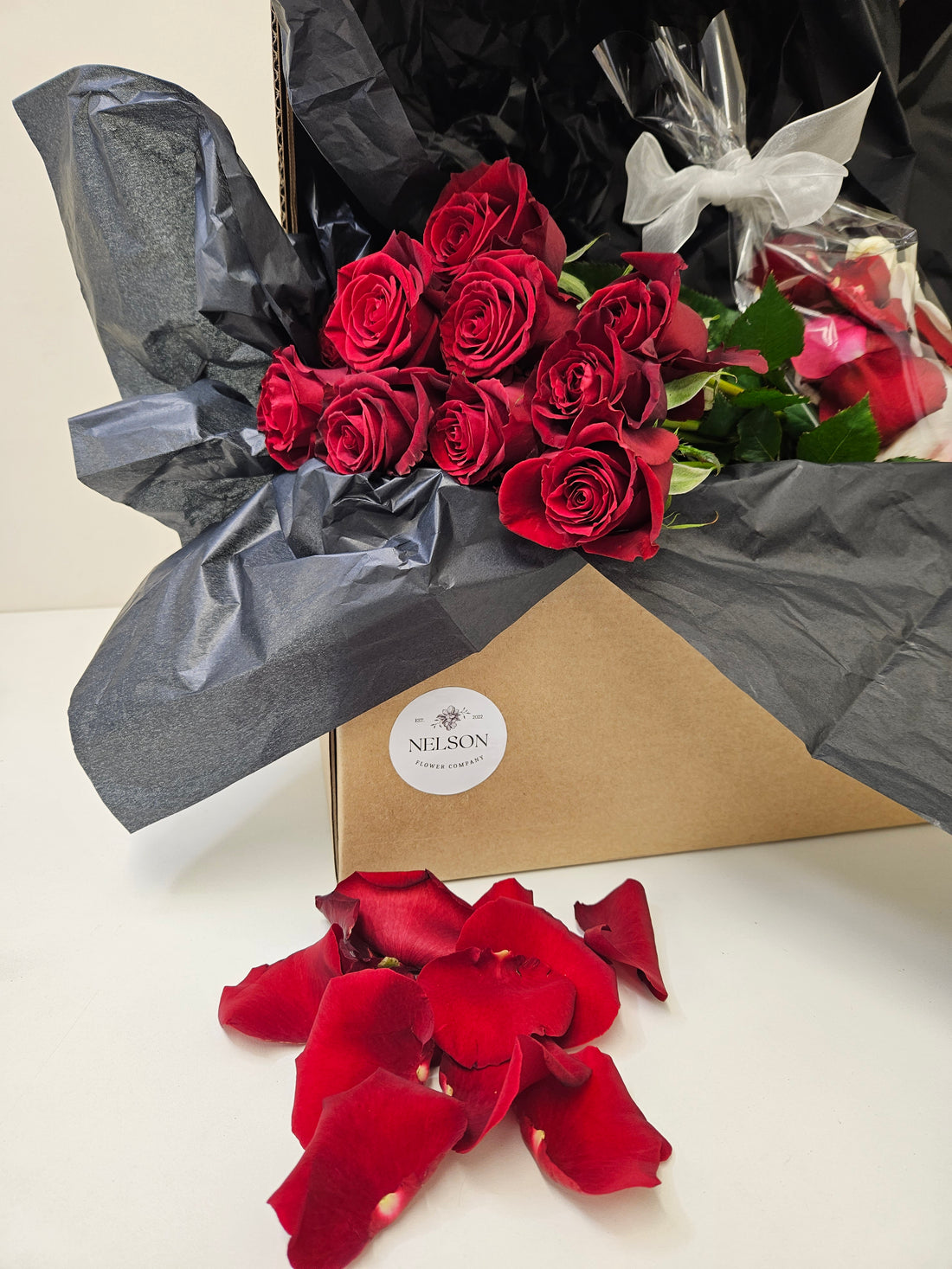 Casanova Box with red roses and matching bundle of Confetti Petals, in cardboard box with black tissue paper.
