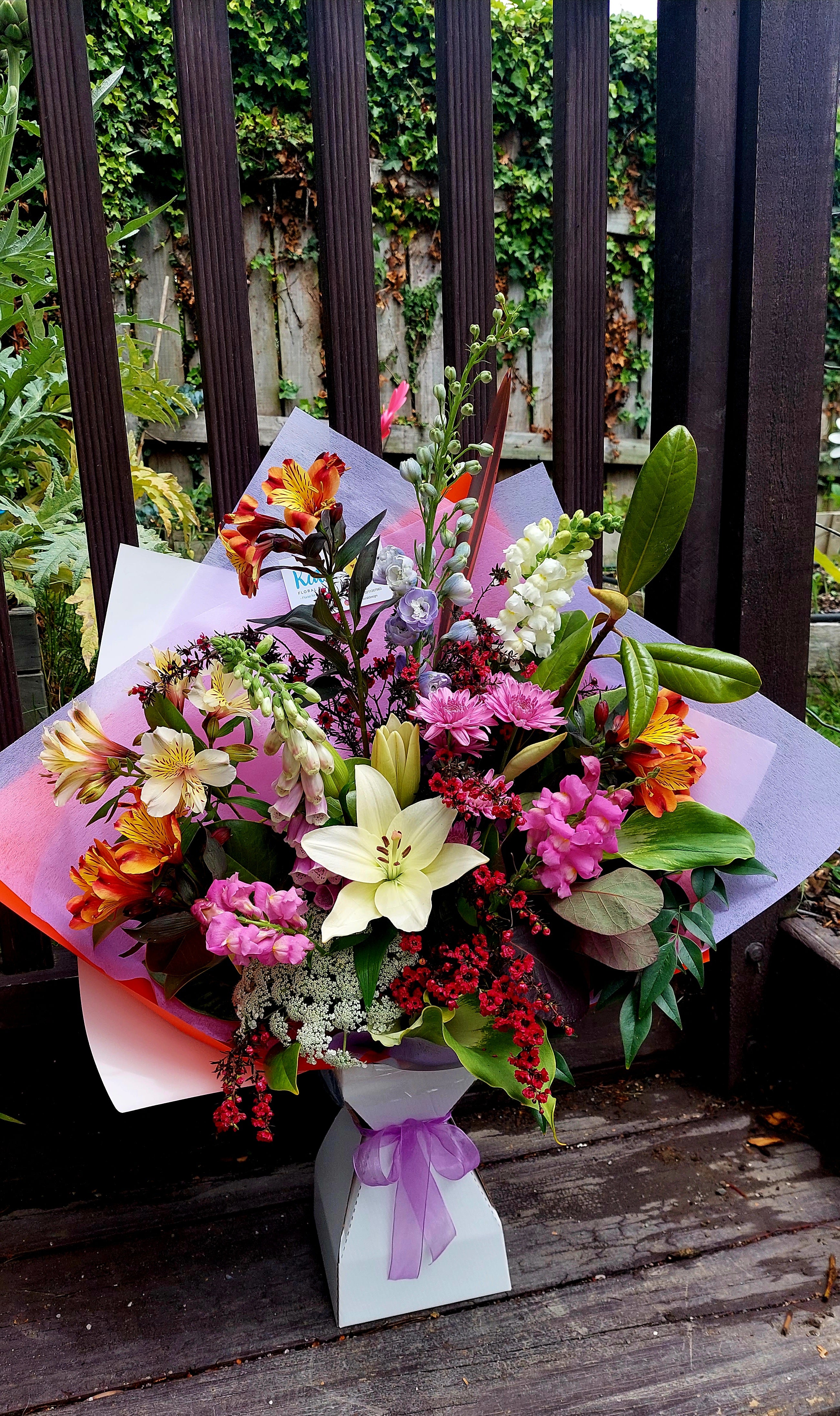 Seasonal Medium Bouquet - Florist Choice with a variety of coloured flowers, wrapped in pink and purple tissue paper.