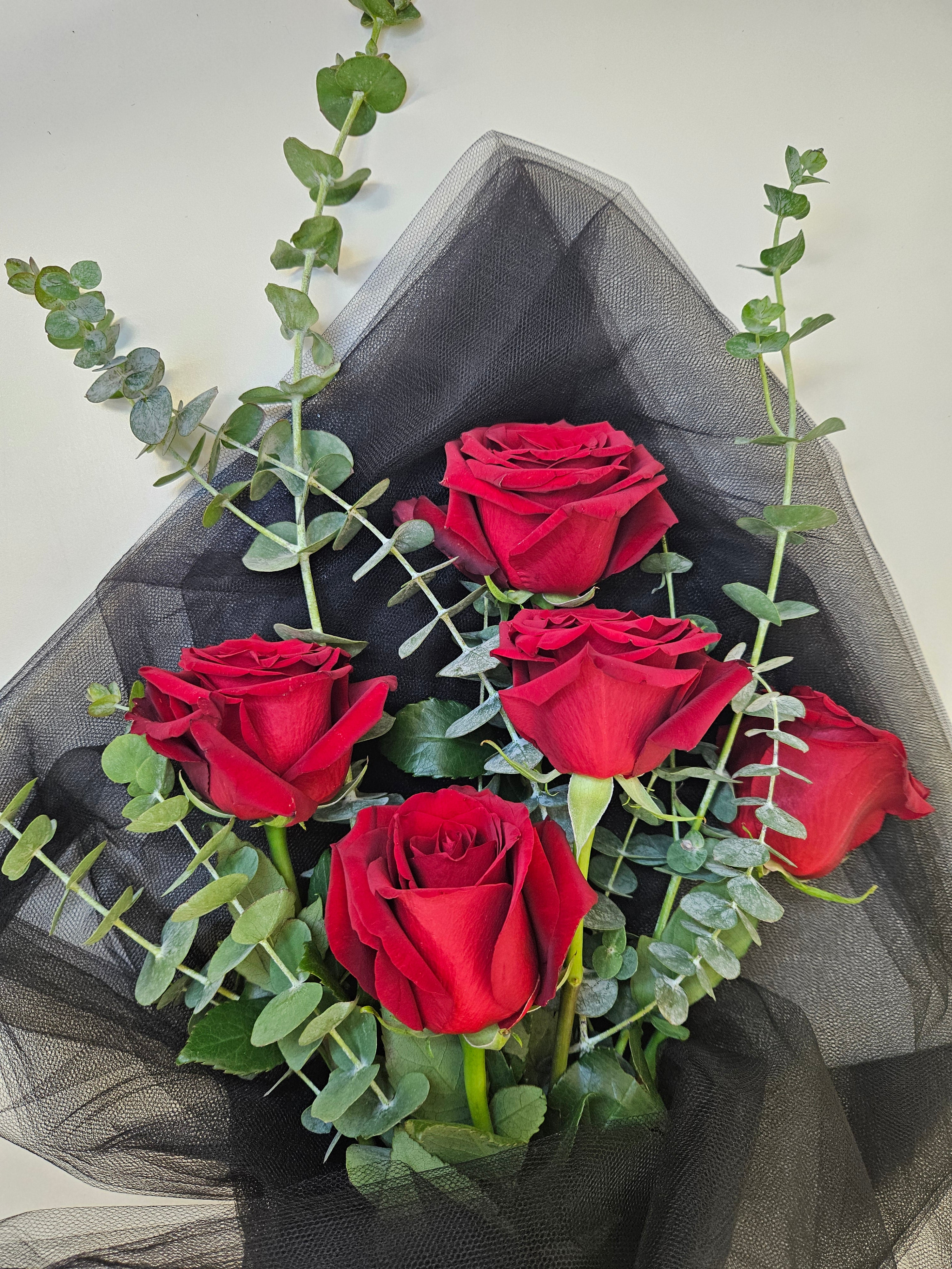 Five long-stemmed roses with foliage wrapped in black.