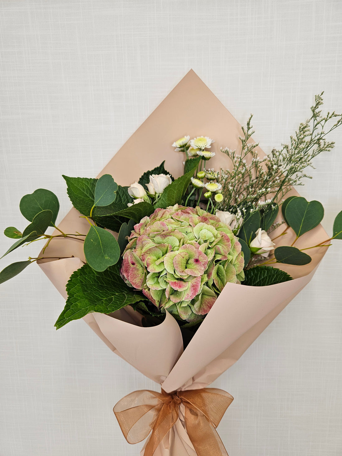 Best Mum Bouquet wrapped in champagne rose gold paper. A floral arrangement made from roses, hydrangeas and more.