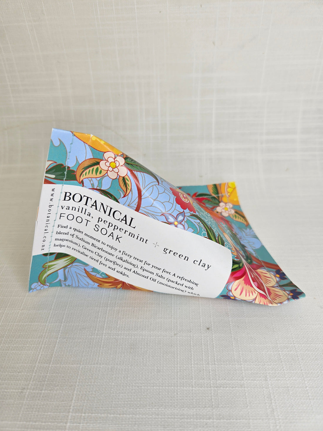 A triangular package of the Botanical Vanilla, Peppermint &amp; Green Clay Foot Soak, with a blue floral pattern.