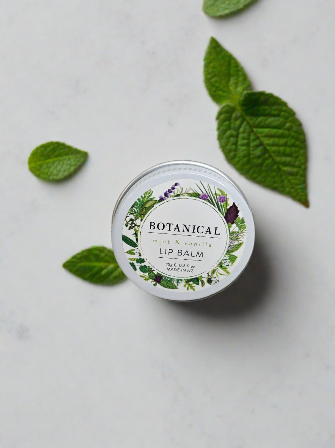 A small tin of the Botanical Mint &amp; Vanilla Lip Balm, with a foliage label.