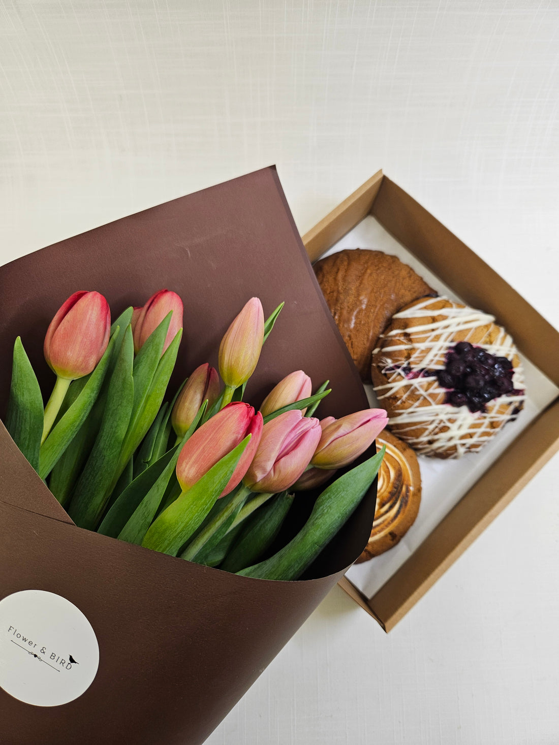 Boujee Bird Biscuit Box with three hand-made cookies in various flavours packaged in a brown carry-box, with a bunch of tulips wrapped in brown paper.