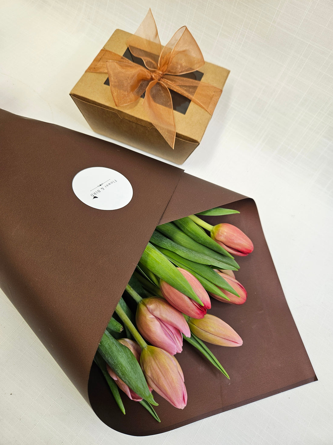 Baby Bird Bliss Box with two Bliss Balls and two Caramel bites topped with edible flowers, packaged in a brown carry-box with a bunch of tulips wrapped in brown paper.