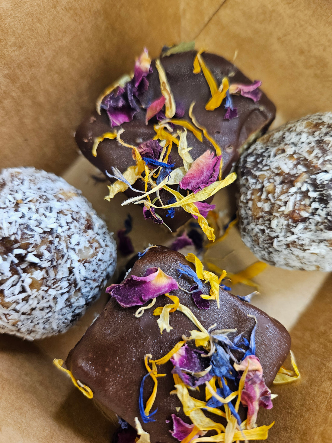 Baby Bird Bliss Box with two Bliss Balls and two Caramel bites topped with edible flowers, packaged in a brown carry-box.