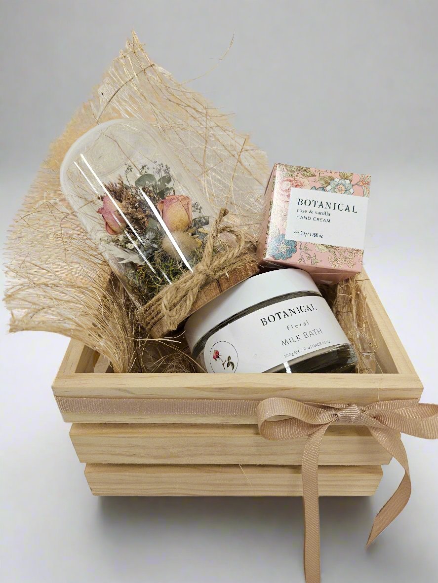 Botanica Box containing a Petite Fleur Dried Floral Dome, Handcream and Milk Bath by Botanical, presented in a wooden crate tied with a champagne ribbon.