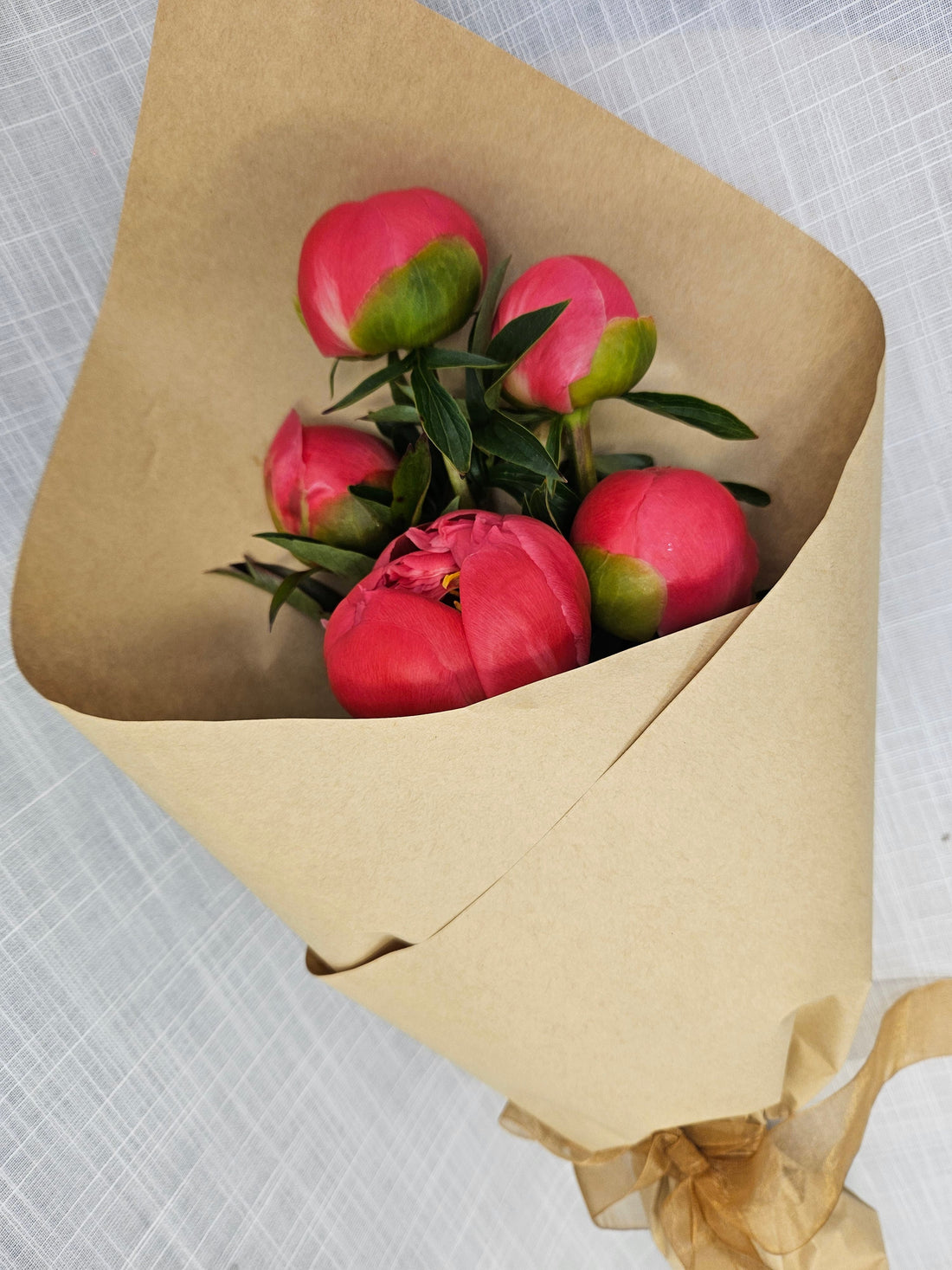 Bunch of pink coral peonies wrapped in brown kraft paper.