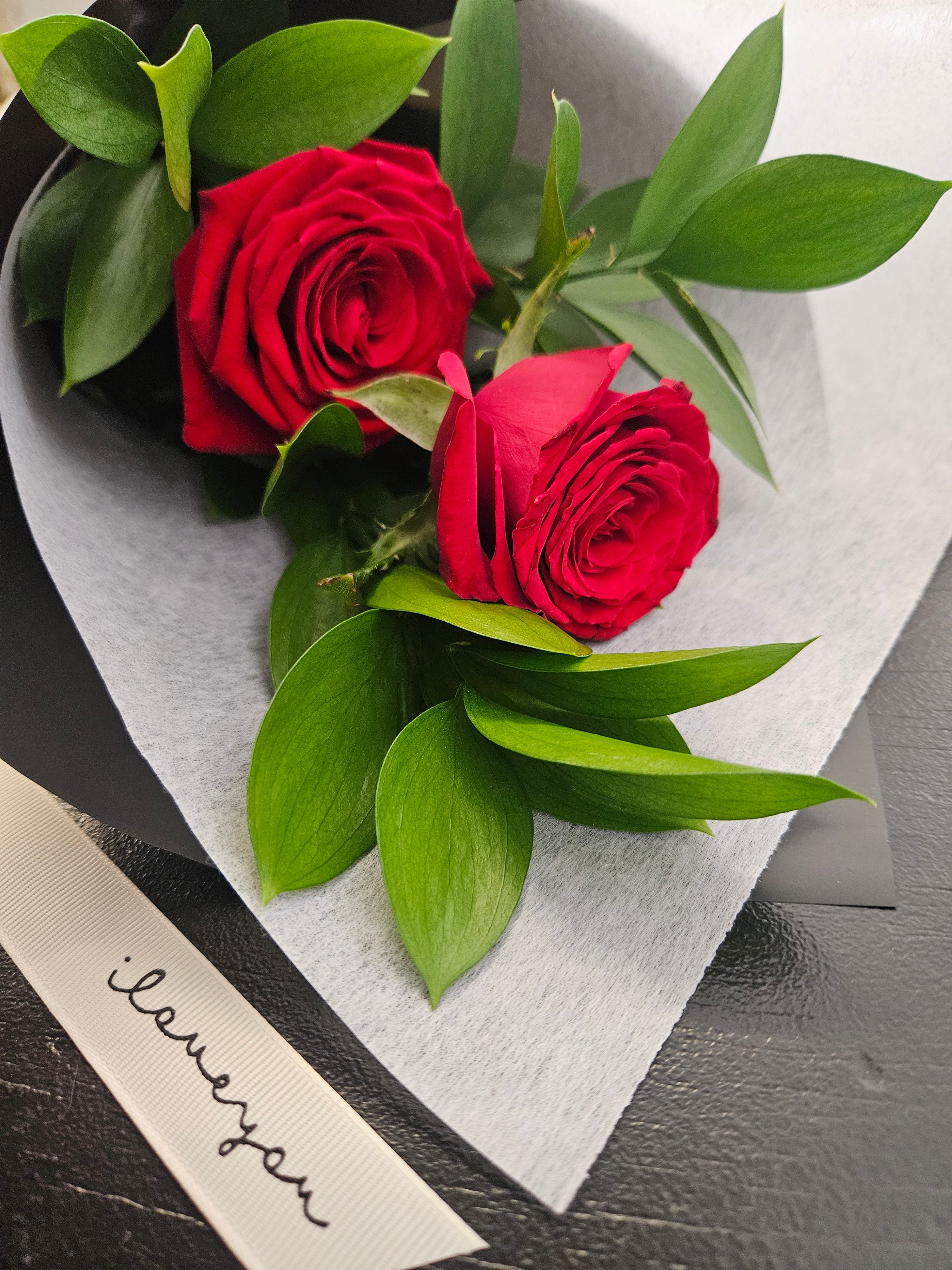 Two of a Kind red rose bouquet wrapped in white and black paper and fabric, tied with a ribbon that reads &