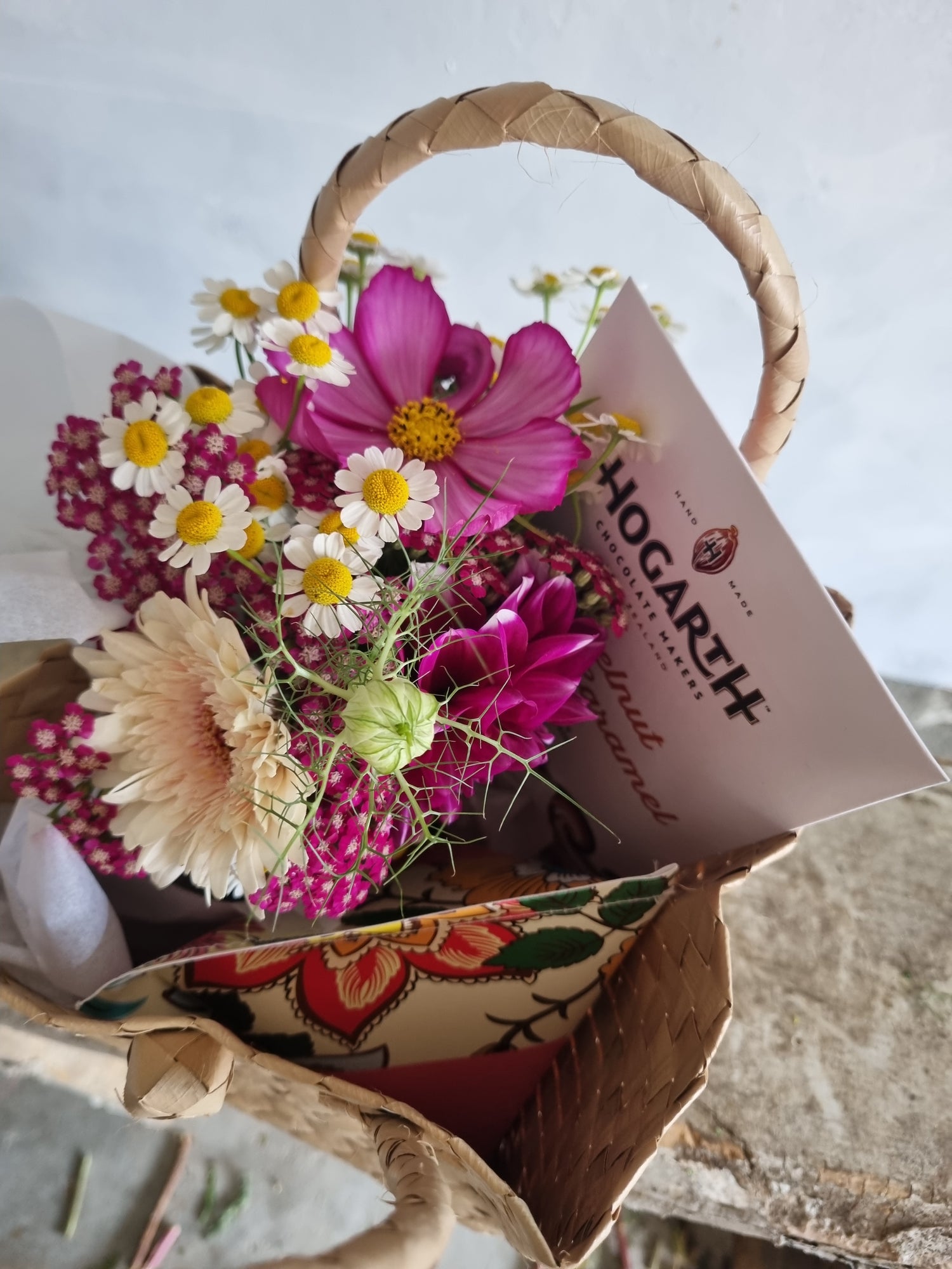 Thinking of You Kete with a pink and white floral posie, Botanical Bath Bomb and bar of Hogarth Chocolate presented in a woven Māori kete (basket).