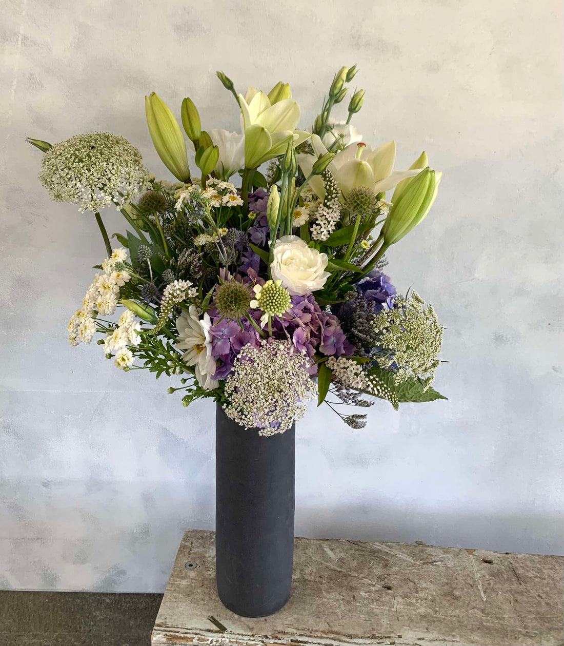 Botanical Beauty floral arrangement made with white, cream and soft purple flowers, presented in a tall black vase.