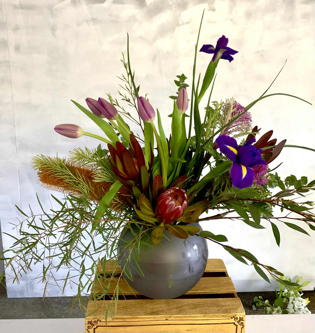 Botanical floral arrangement made with a variety of seasonal blooms and foliage, presented in a frosted fish bowl vase.