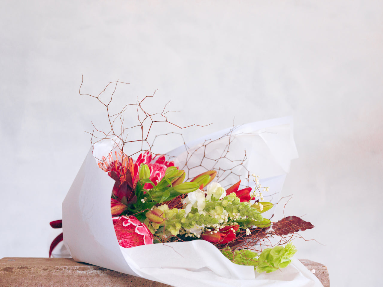 Feeling Festive Christmas bouquet made with red and green flowers and foliage, wrapped in white paper and tied with a matching ribbon.