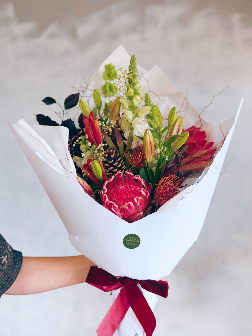 Feeling Festive Christmas bouquet made with red and green flowers and foliage, wrapped in white paper and tied with a matching ribbon.