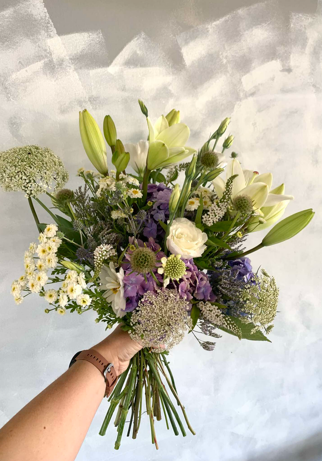 Botanical Beauty floral arrangement made with white, cream and soft purple flowers, presented in a tall black vase.