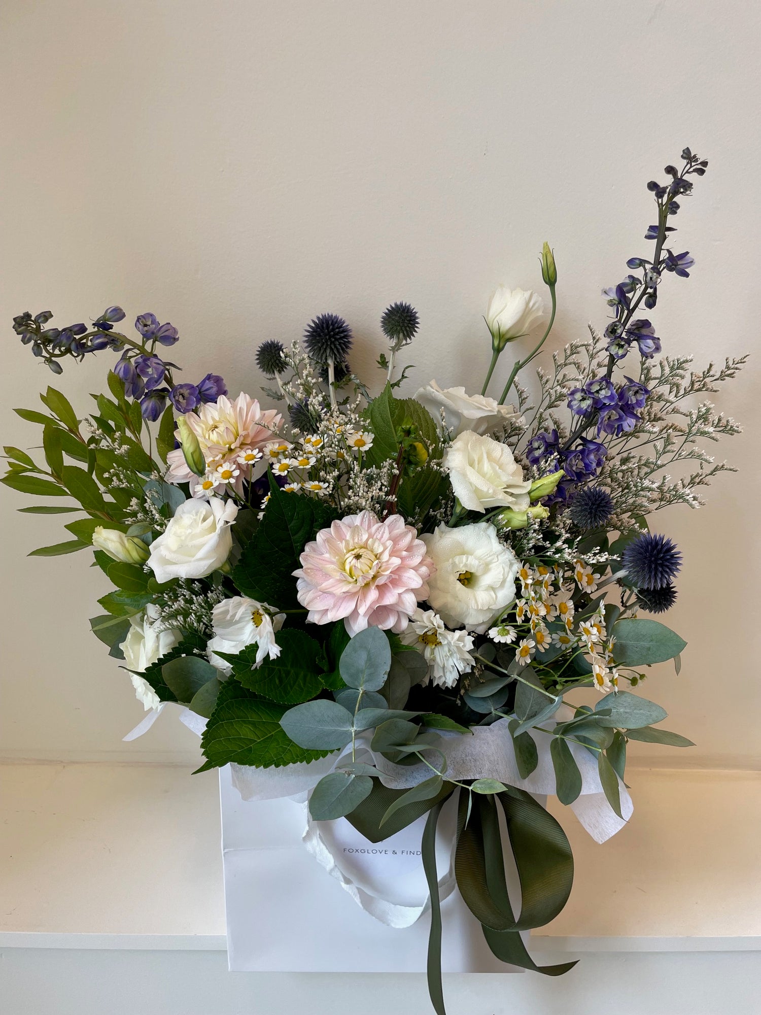 The Sympathy Box floral bouquet made with flowers in soft white and pastel tones with greenery, presented in a white carry box.