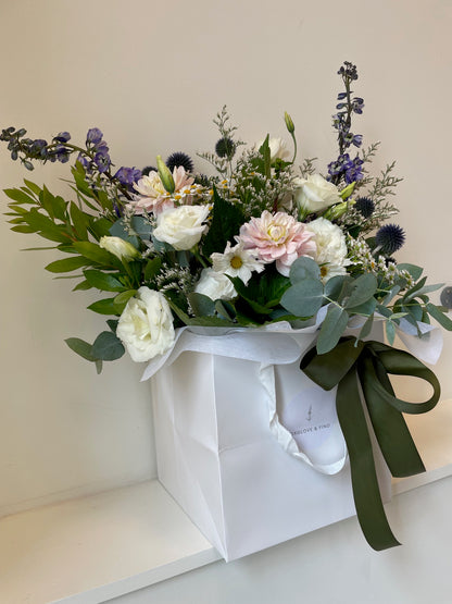 The Sympathy Box floral bouquet made with flowers in soft white and pastel tones with greenery, presented in a white carry box.