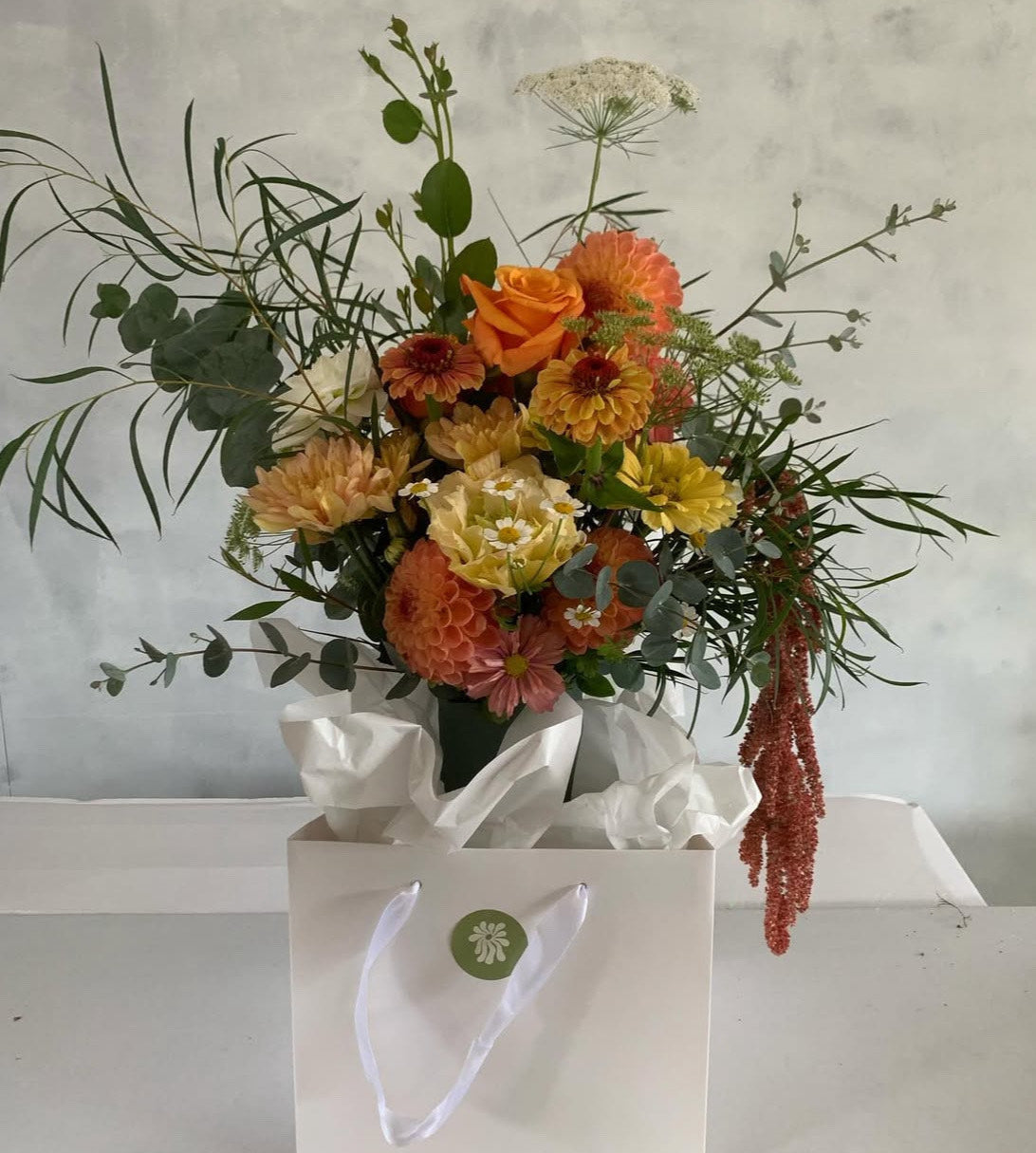 Glow floral bouquet made with vibrant yellow, orange and white flowers and foliage, presented in a green ceramic Ned vase.