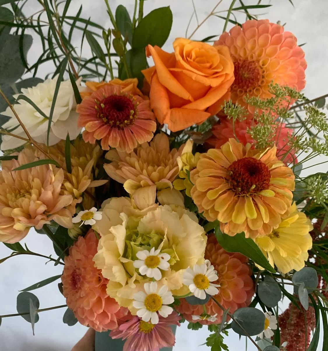 Close-up of Glow floral bouquet made with vibrant yellow, orange and white flowers and foliage, presented in a green ceramic Ned vase.