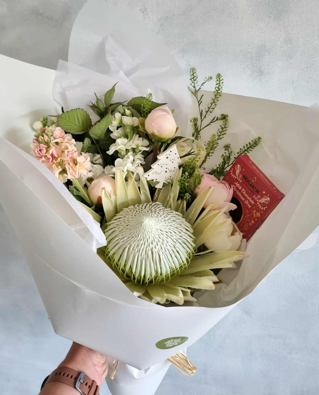 White Christmas bouquet made with white and rosy pink flowers and foliage, wrapped in matching paper. Complete with chocolate and Christmas ornament.