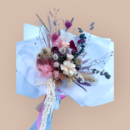 Eternal Petals bouquet with neutral-toned flowers and foliage, wrapped in white paper against a beige backdrop.