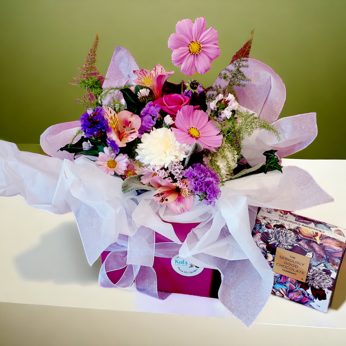 Posy of vibrant pink, purple and white flowers, arranged in a pink box with ribbon and tissue paper. 