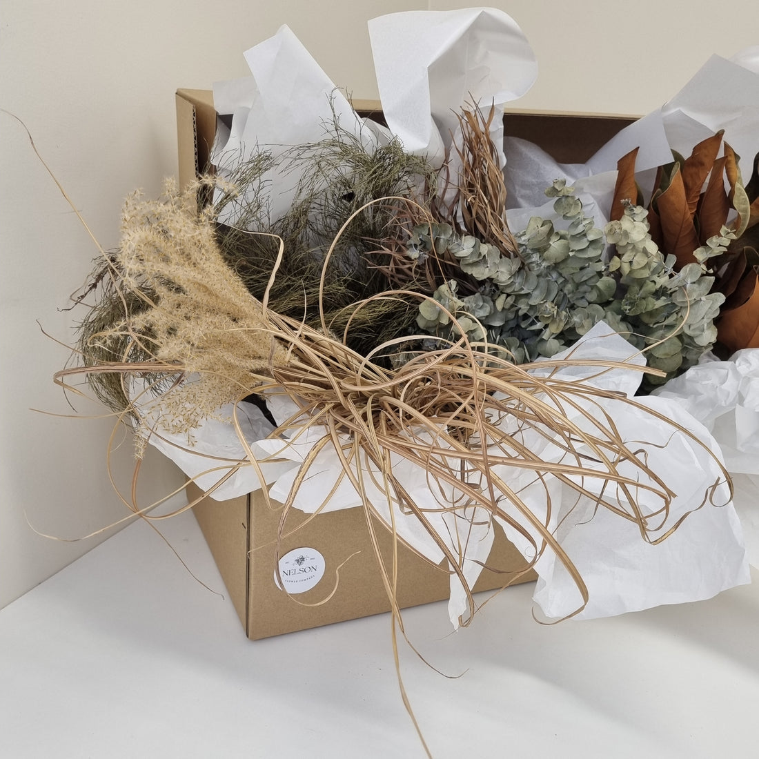 Dried Foliage Box filled with various preserved greenery, in a cardboard box with white tissue paper.