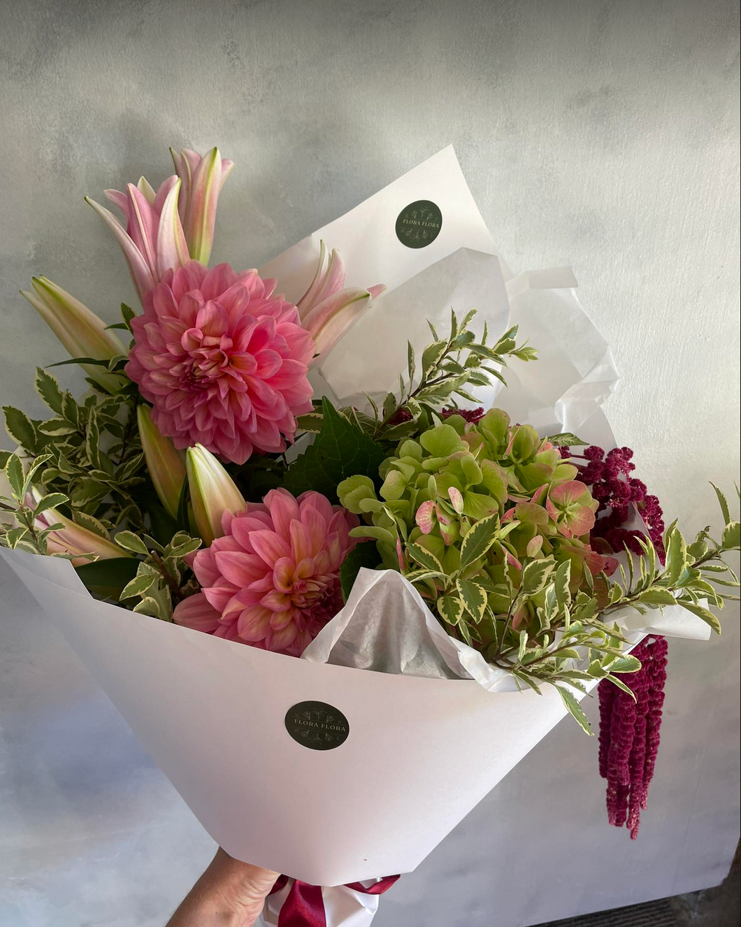 An example of what your Seasonal Bunch from Flora Flora could look like. Pink and green flowers with greenery, wrapped in white paper.