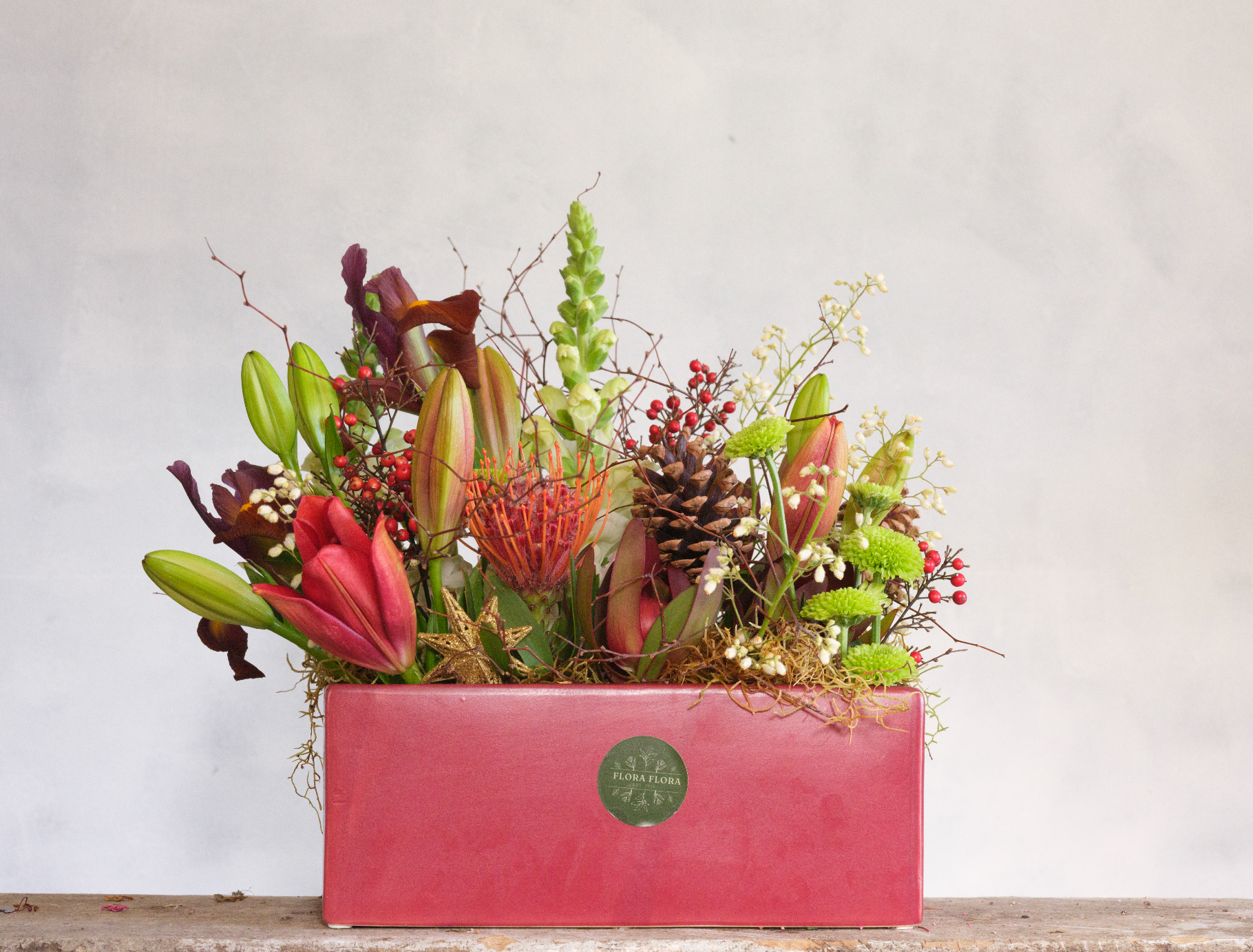 Jingle Bells floral arrangement made with festive red and green flowers and foliage, presented in a red ceramic vase.