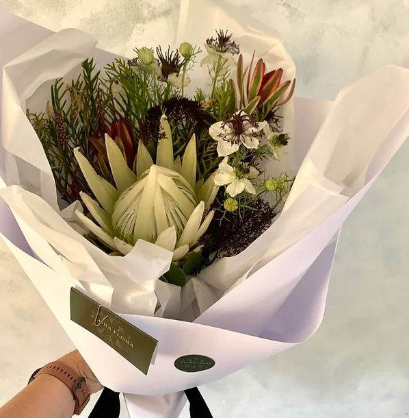 Let It Snow bouquet made with white protea flowers and green foliage, wrapped in white paper tied with a matching bow.